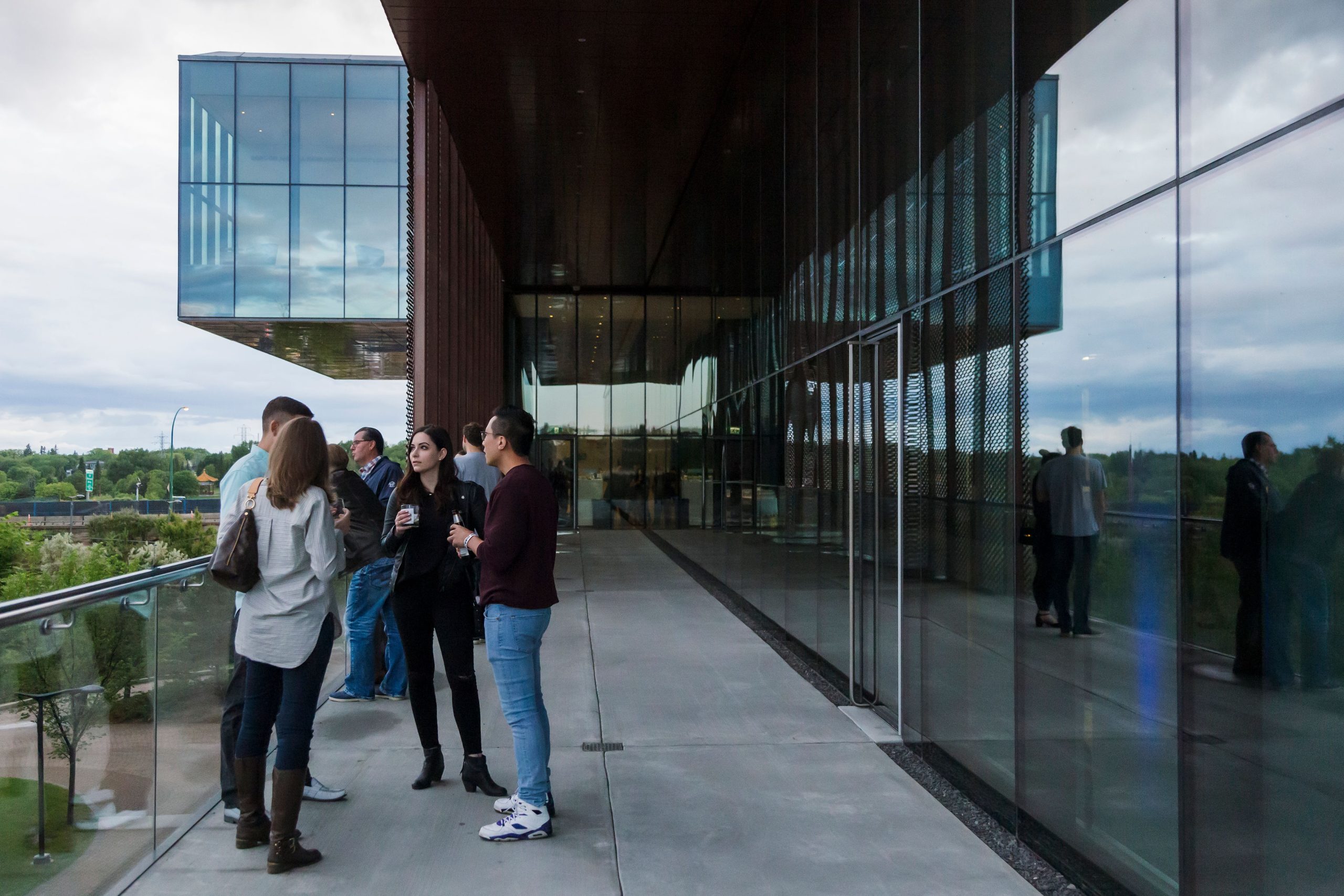 A group of people stand on Remai Modern's Level 2 balcony, from which you can see the museum's cantilevered floors jutting out from Level 4.