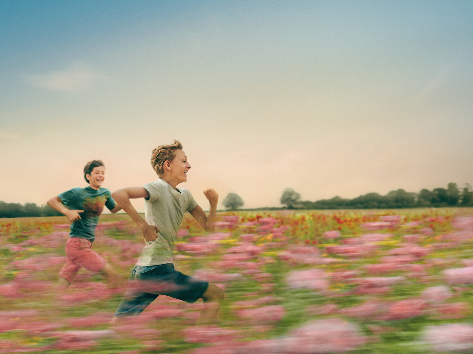 Two children run in a field of flowers.