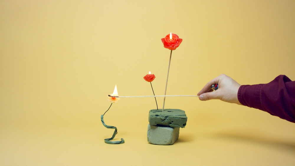 A hand lighting a candle in the shape of a rose