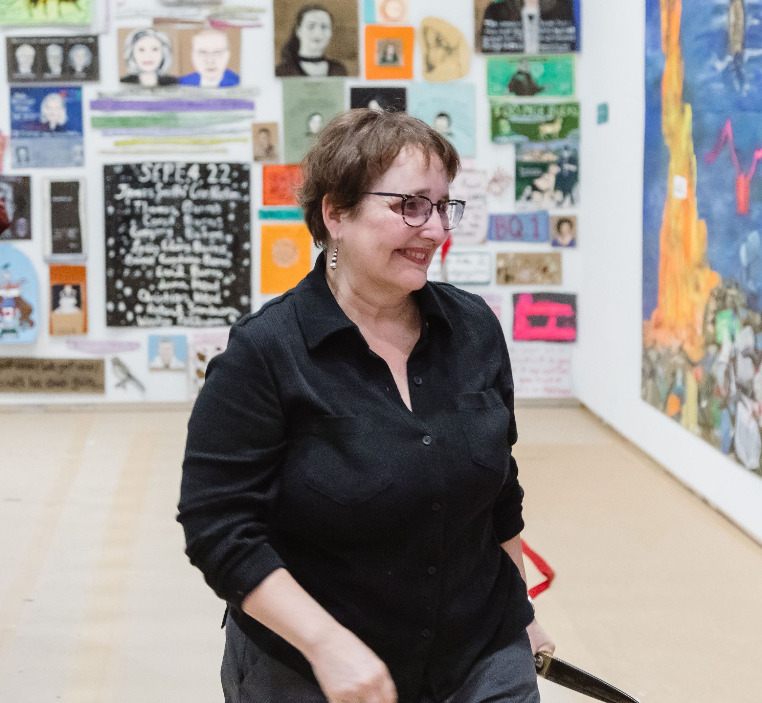 Artist Betsy Rosenwald is pictured in her collaborative exhibition with Dawna Rose called Journal of the Plague Year(s) at Remai Modern. Dozen of paintings on cardboard featuring varied subject matter can be seen in the background.