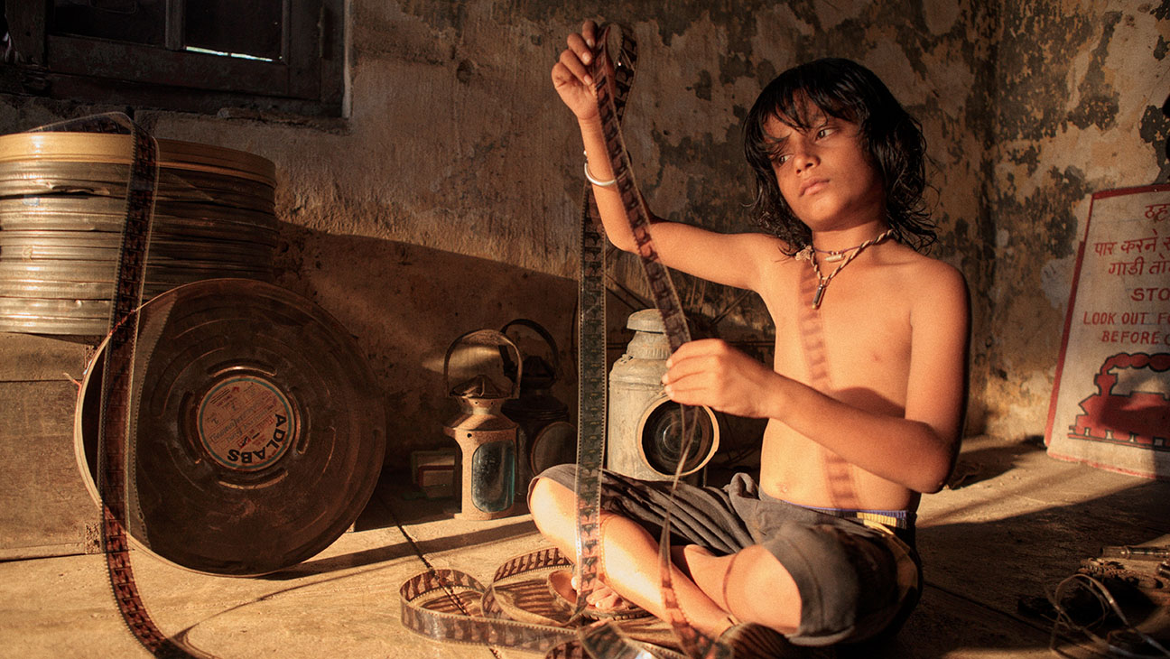 "A young boy, sitting on the floor of a dimly lit room, carefully handling a strip of film.