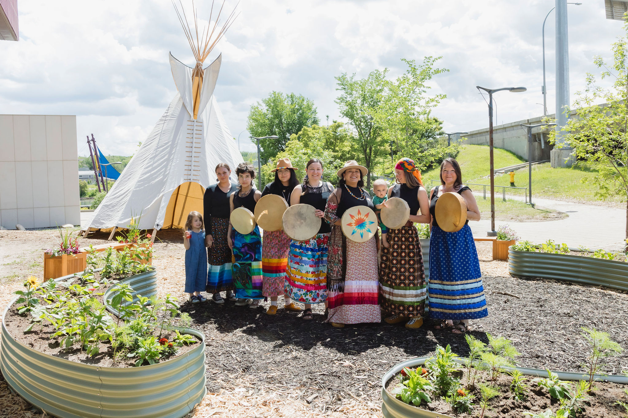 A group of people stand outside Remai Modern on a summer day in front of a tipi.