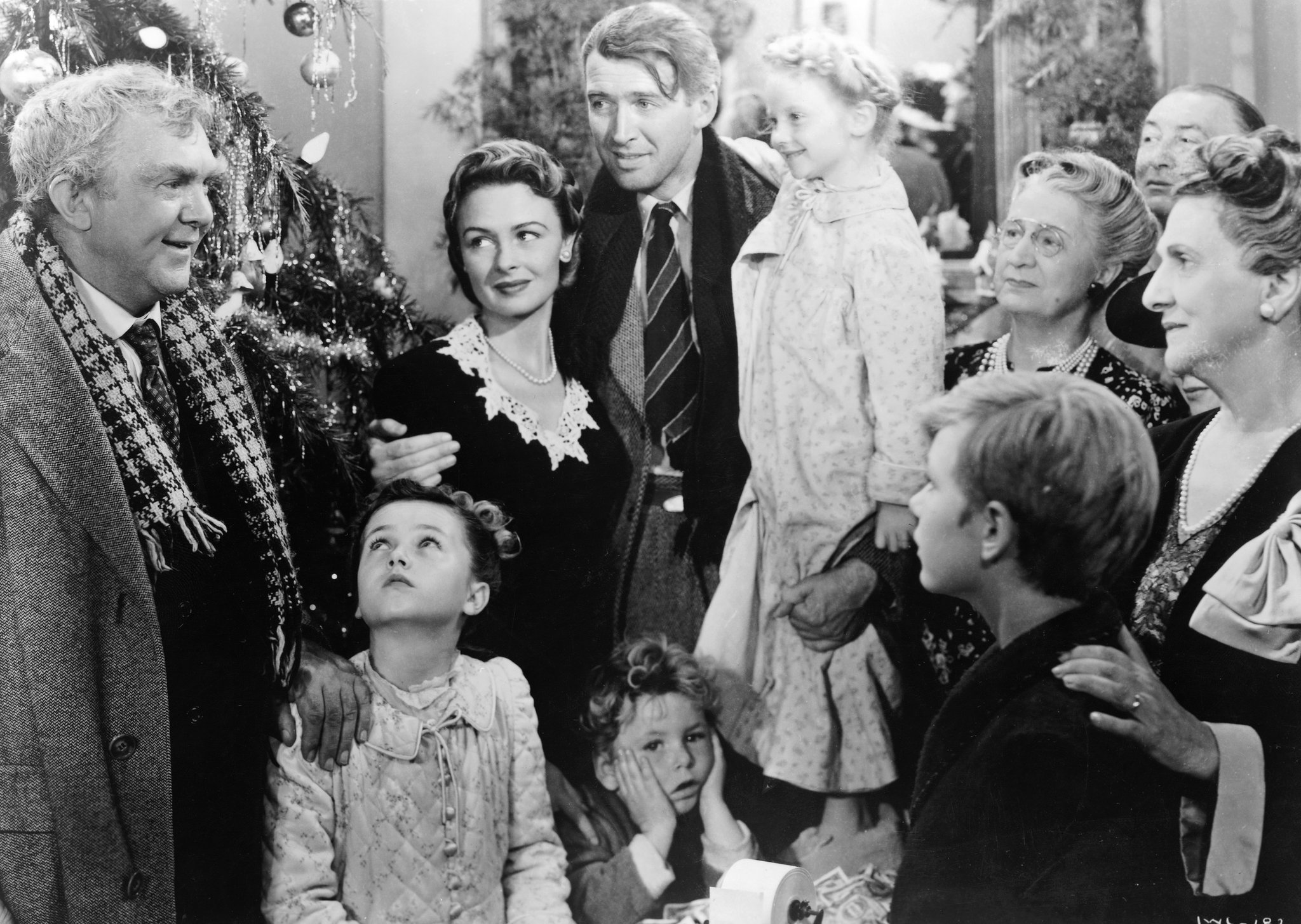 "Vintage black and white photo of a group gathering, possibly a family, near a Christmas tree."