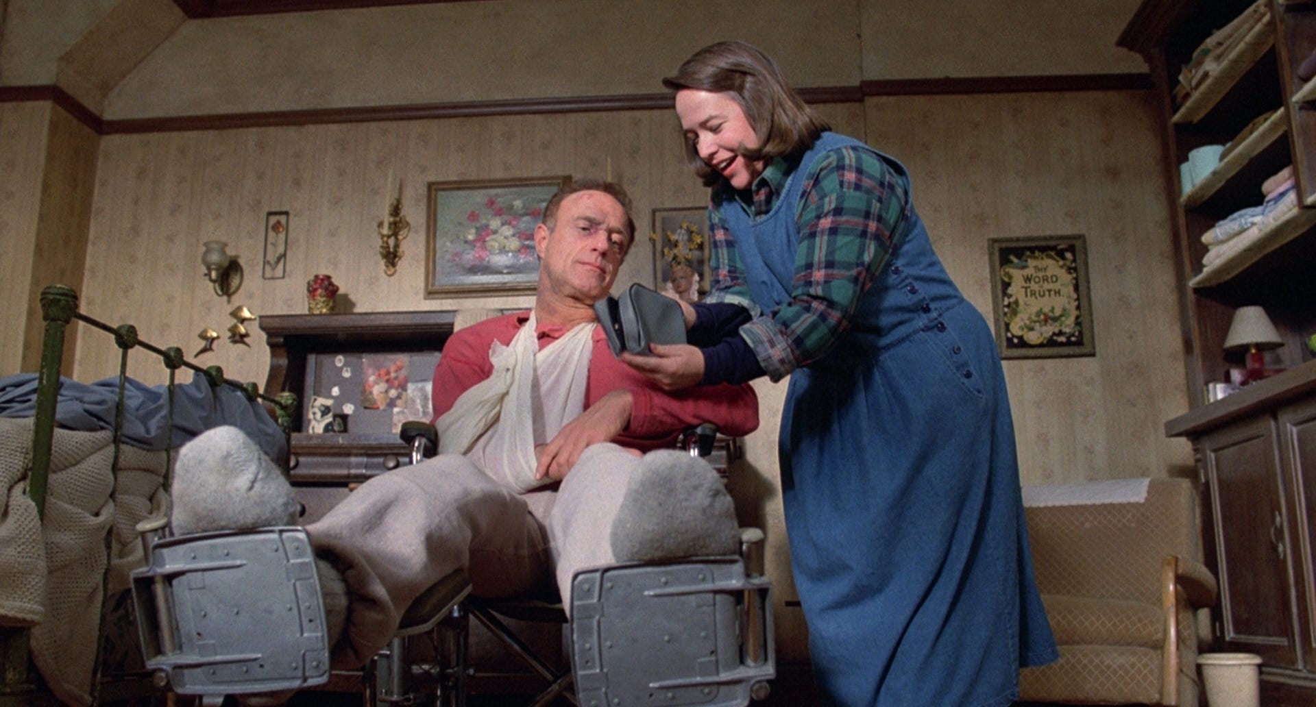 "A person in a wheelchair with a leg cast and sling, as another person attends to them in a vintage room."