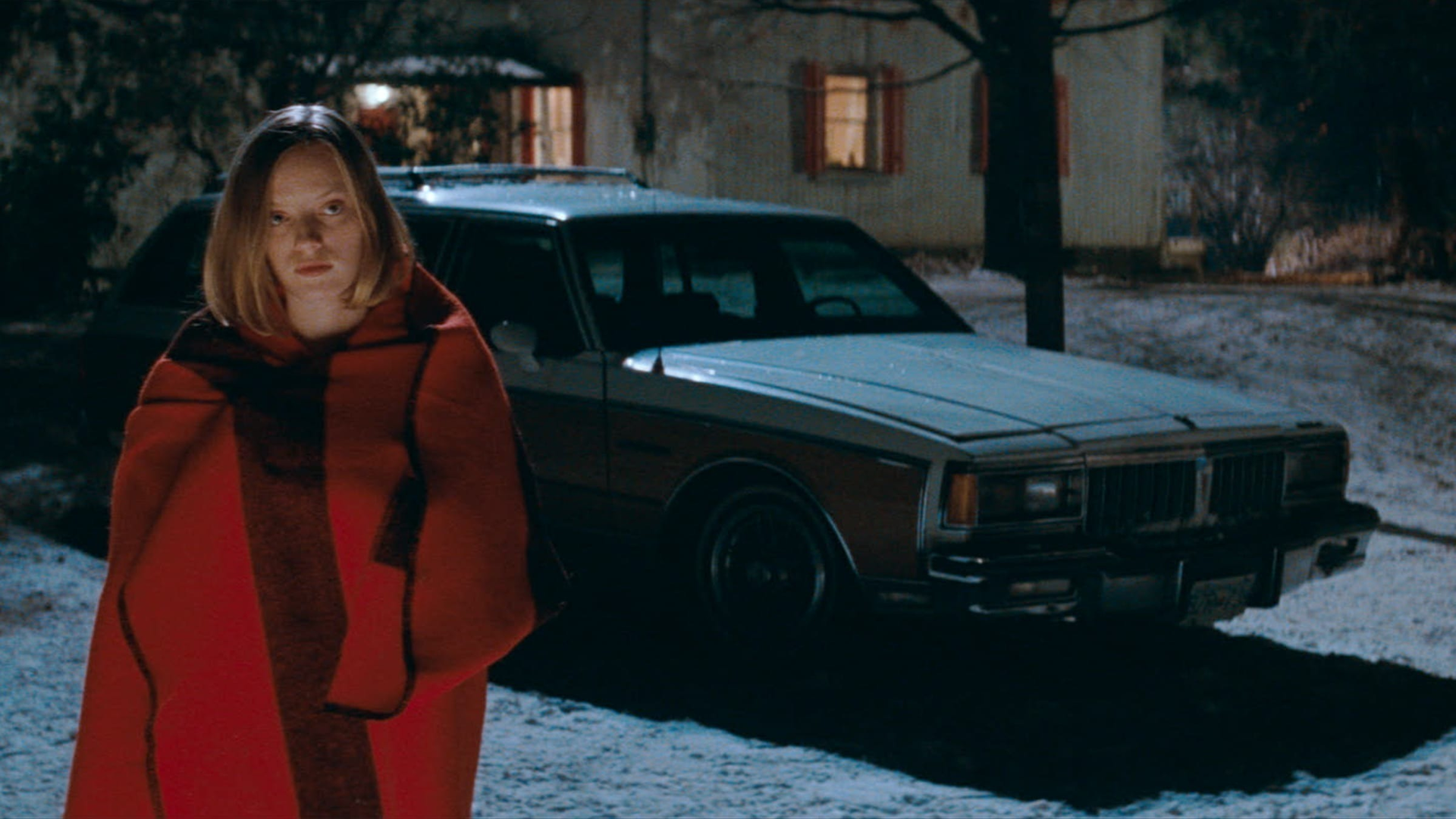 "A photo of a lady standing in the cold covered with a red blanket"