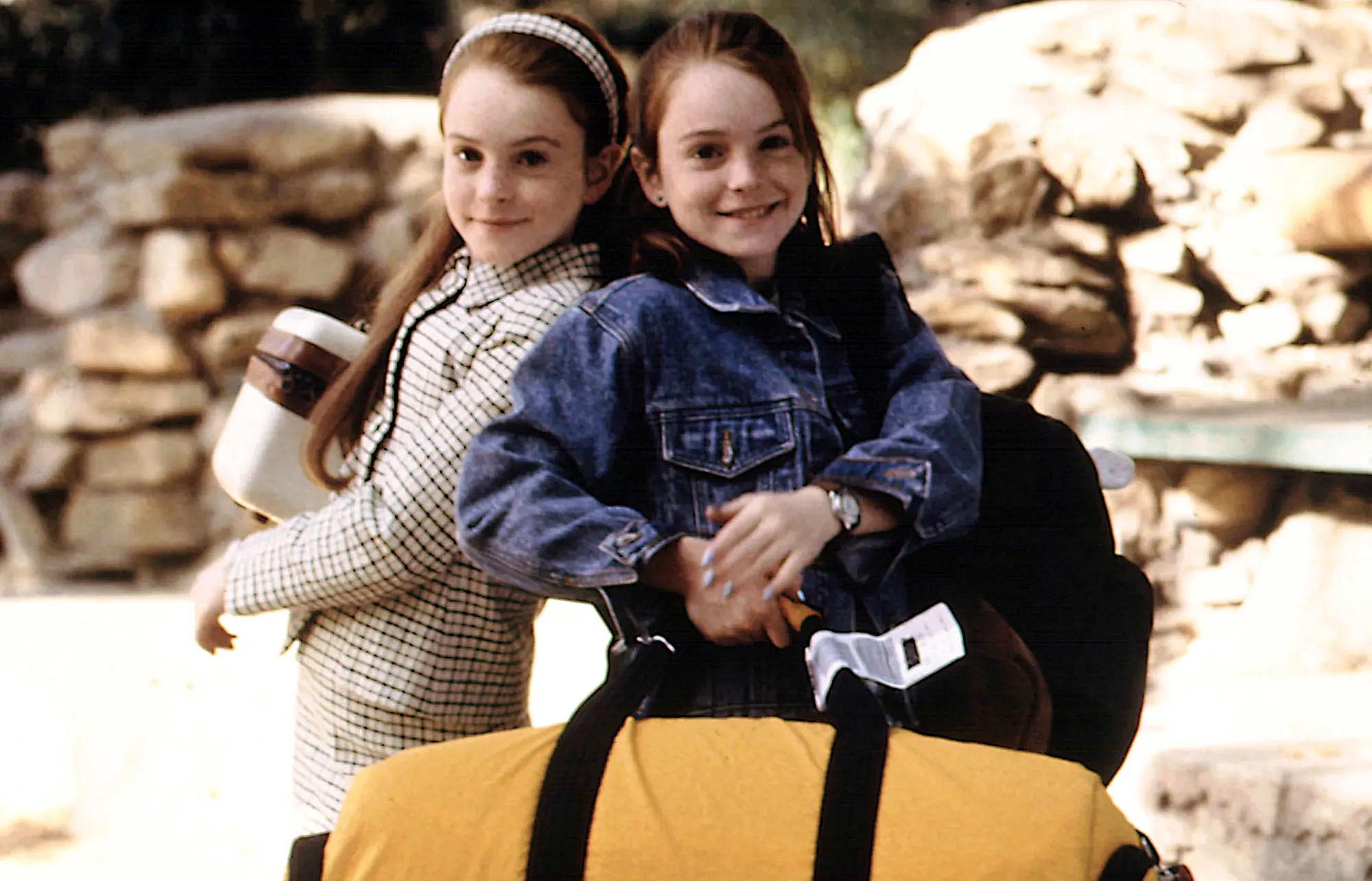 Two young girls stand beside a suitcase, smiling and enjoying their time together in a cheerful setting.