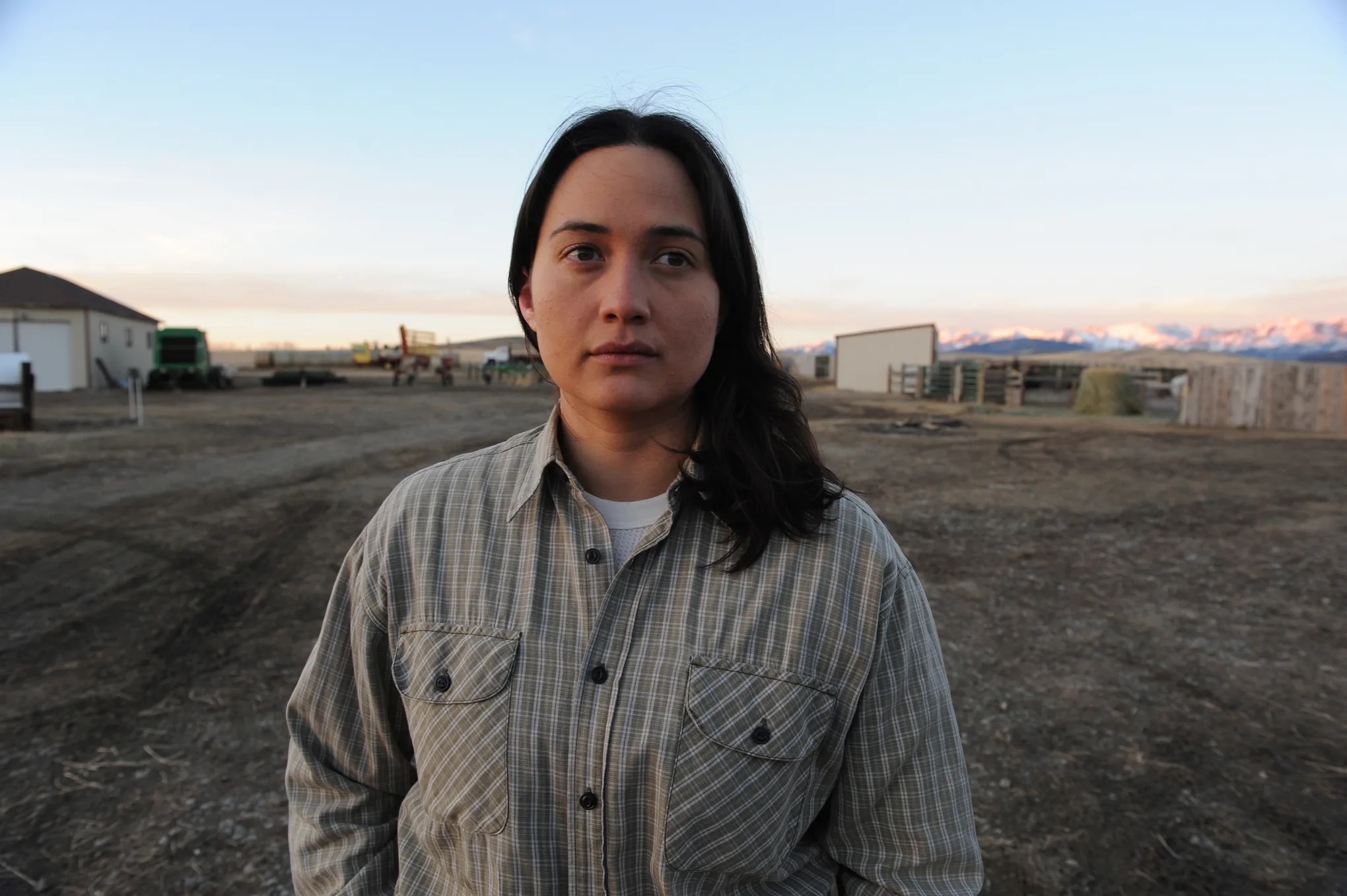 A woman stands confidently in front of a vast field, showcasing her connection to the land.