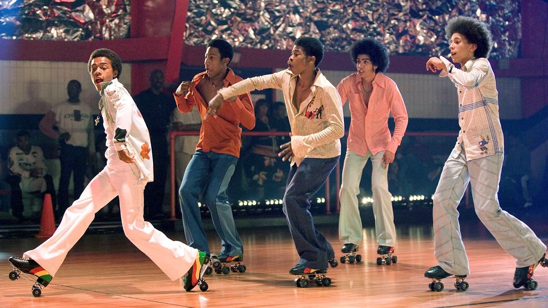 Five people roller skating on a wooden floor in colorful 70s attire, performing a synchronized dance routine.