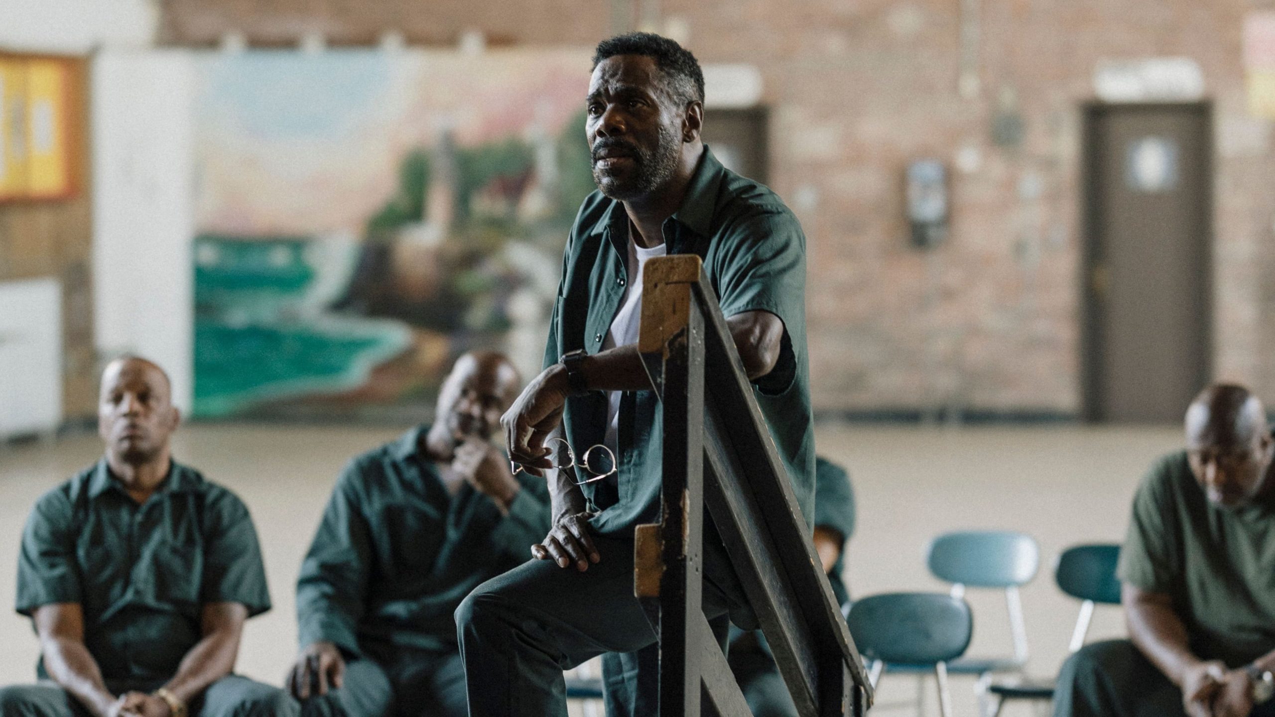 A man sitting before a gathering of men, indicating a moment of dialogue or interaction among peers in a formal context.