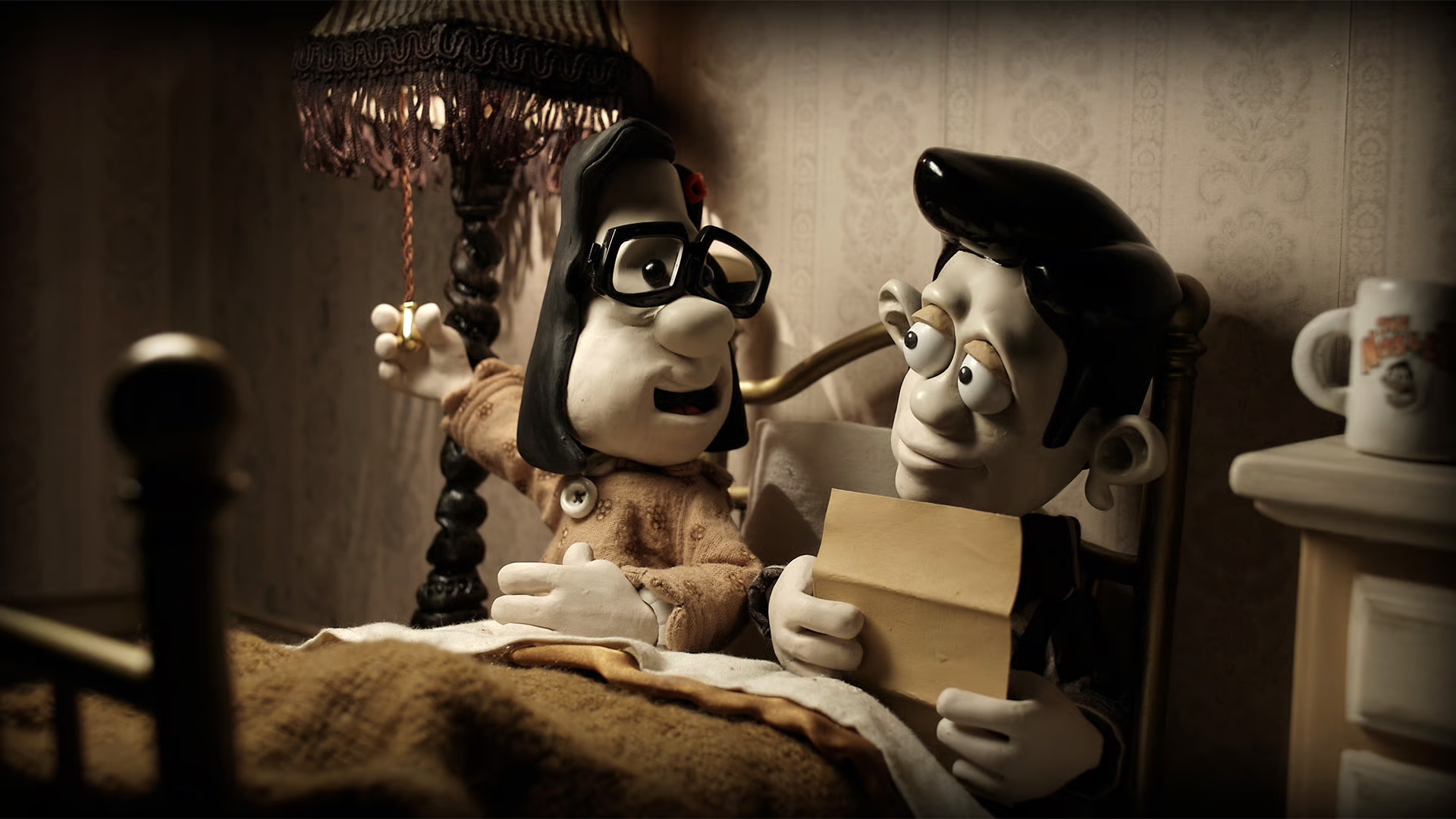 Claymation-style characters sit in bed under a brown blanket in a dimly lit, vintage-styled bedroom. One character, wearing glasses and a nightgown, reaches up to pull a cord on a fringed lamp. The other holds an envelope and looks at them with wide eyes. A mug with a cartoon face sits on a nightstand beside the bed.