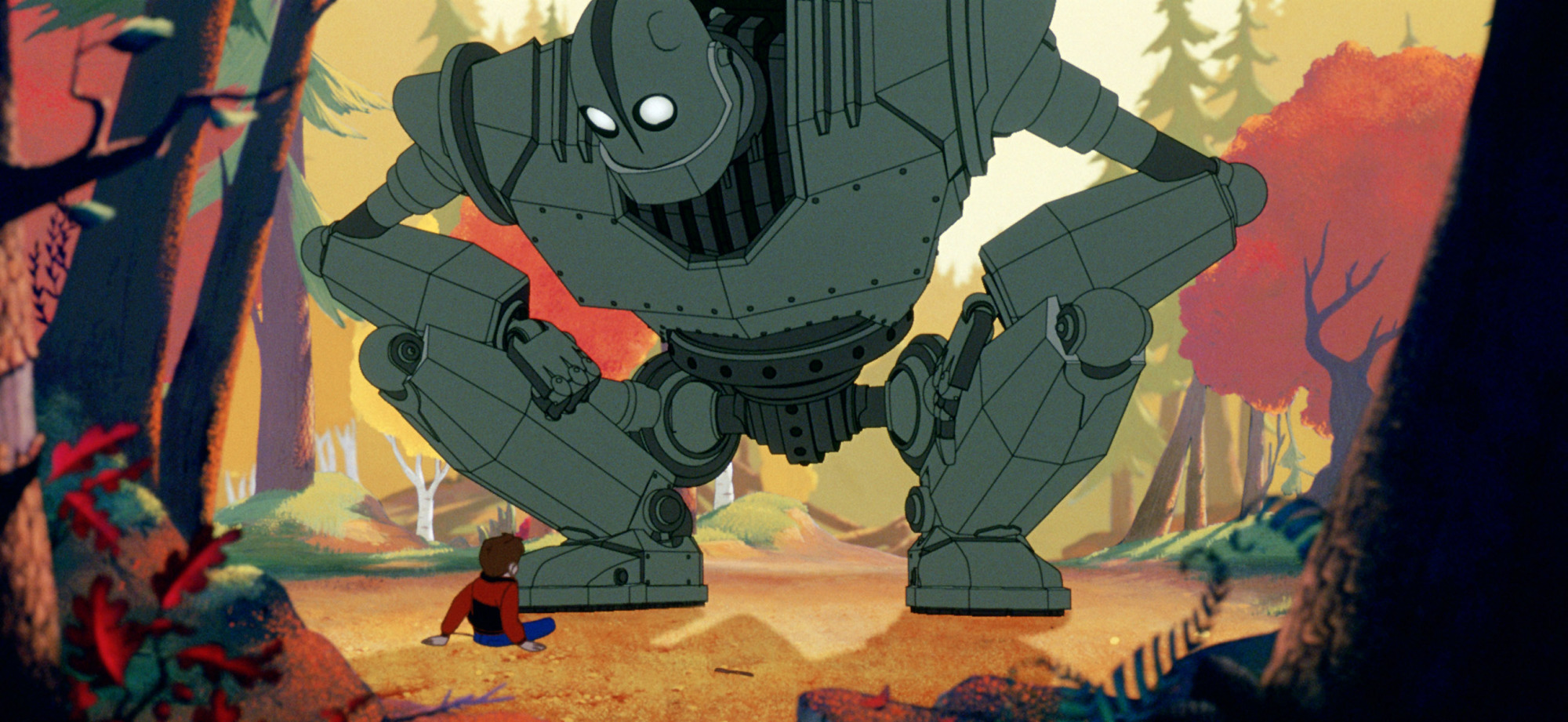 An animated scene shows a massive gray robot crouching in a colorful forest clearing, its glowing white eyes focused downward. In front of it, a small child sits on the ground, looking up at the towering figure. Tall trees with autumn-coloured leaves surround them.